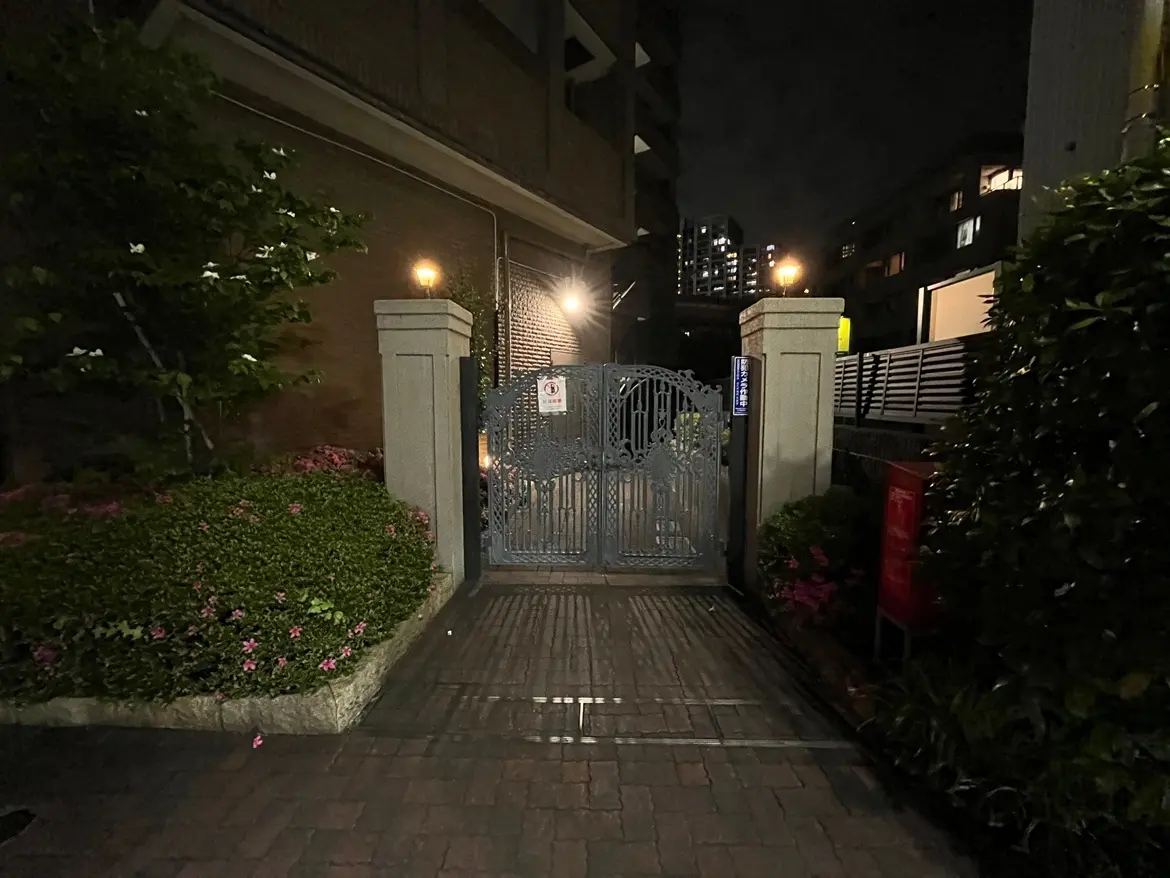- 夜間のエントランスゲート、緑豊かな植栽と明るい照明がある住宅街の入口の風景