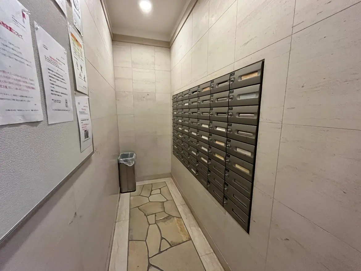 - 高級マンションの共用スペース、壁に設置された郵便受けと掲示板、清掃された床のエントランスエリア