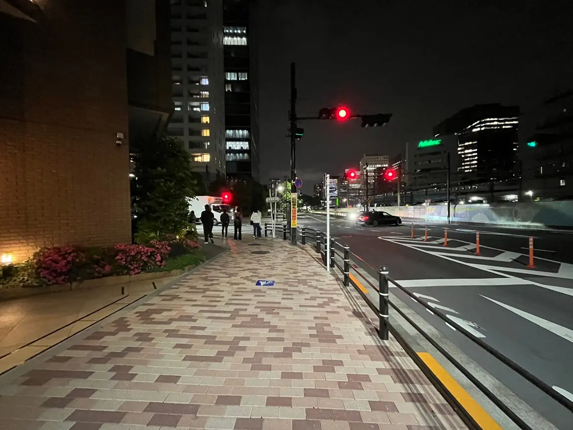 - 夜の都市景観、信号機が赤信号になっている交差点と歩道、周囲に立つビルと街灯の明かり