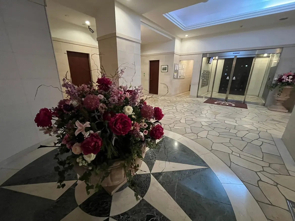 - エレベーターの前に置かれた華やかな花のアレンジメントと石材の床、明るいロビーのインテリアデザイン