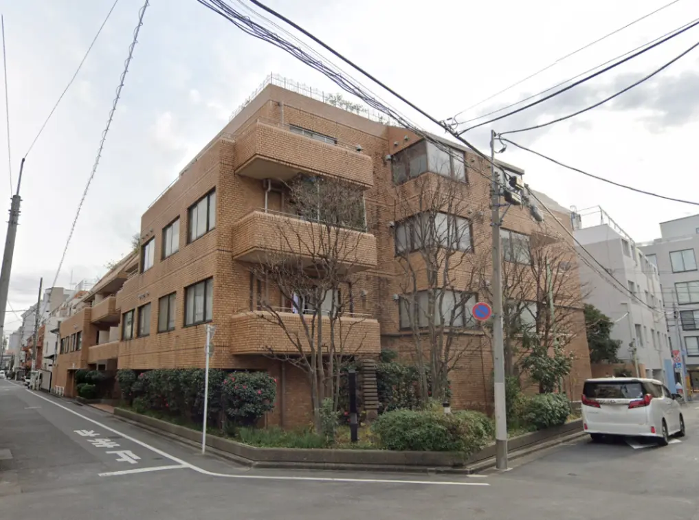 - レンガ造りのマンションの外観、周囲に緑豊かな植栽と街の風景、道路沿いの様子を捉えた写真