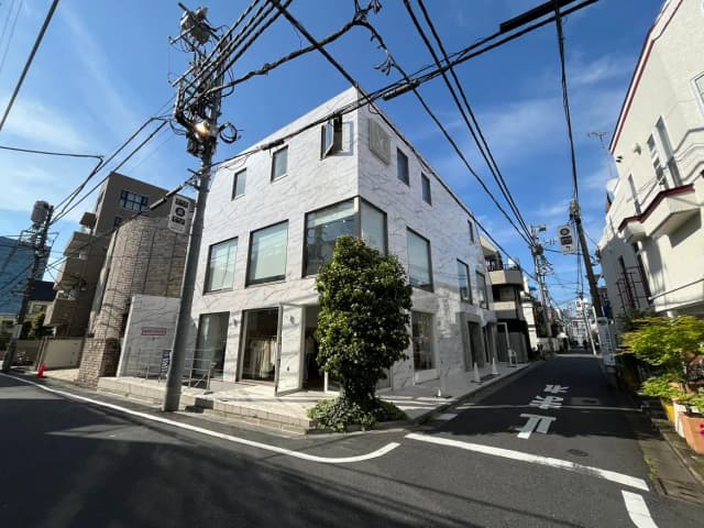 - 白い外壁のモダンな建物が並ぶ静かな街角、青空と電線が交差する様子