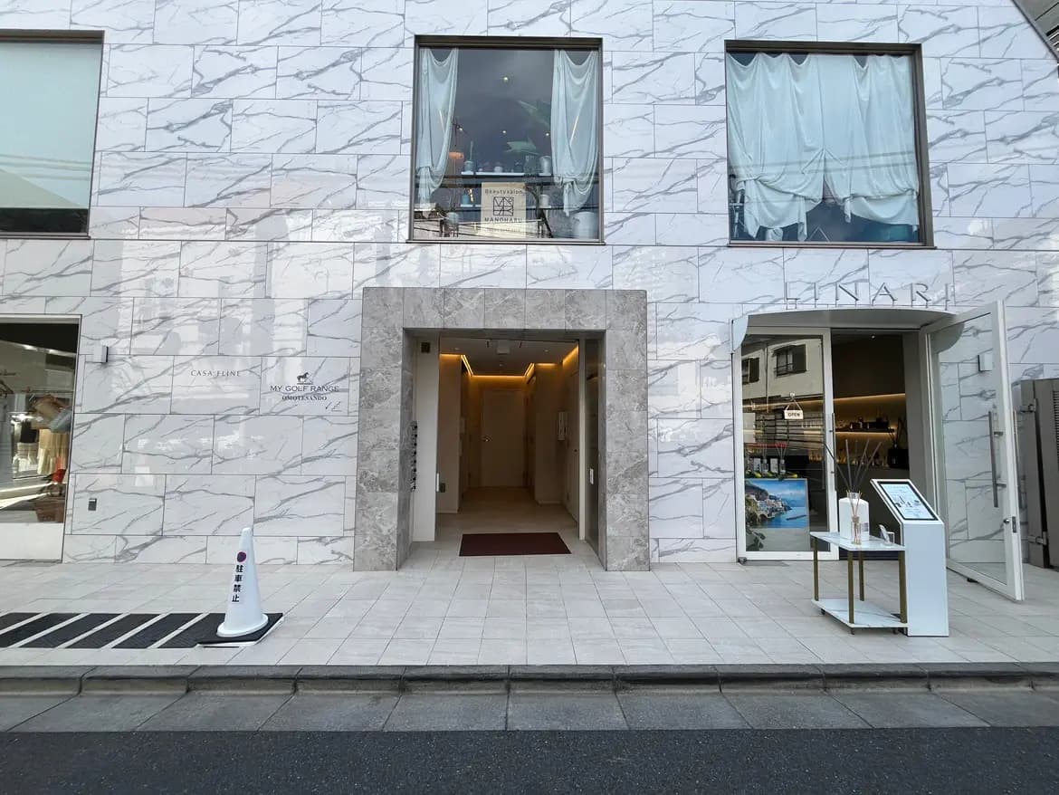 - モダンな外観の建物入口、マーブル調の壁、周囲にある店舗の窓と歩道の様子