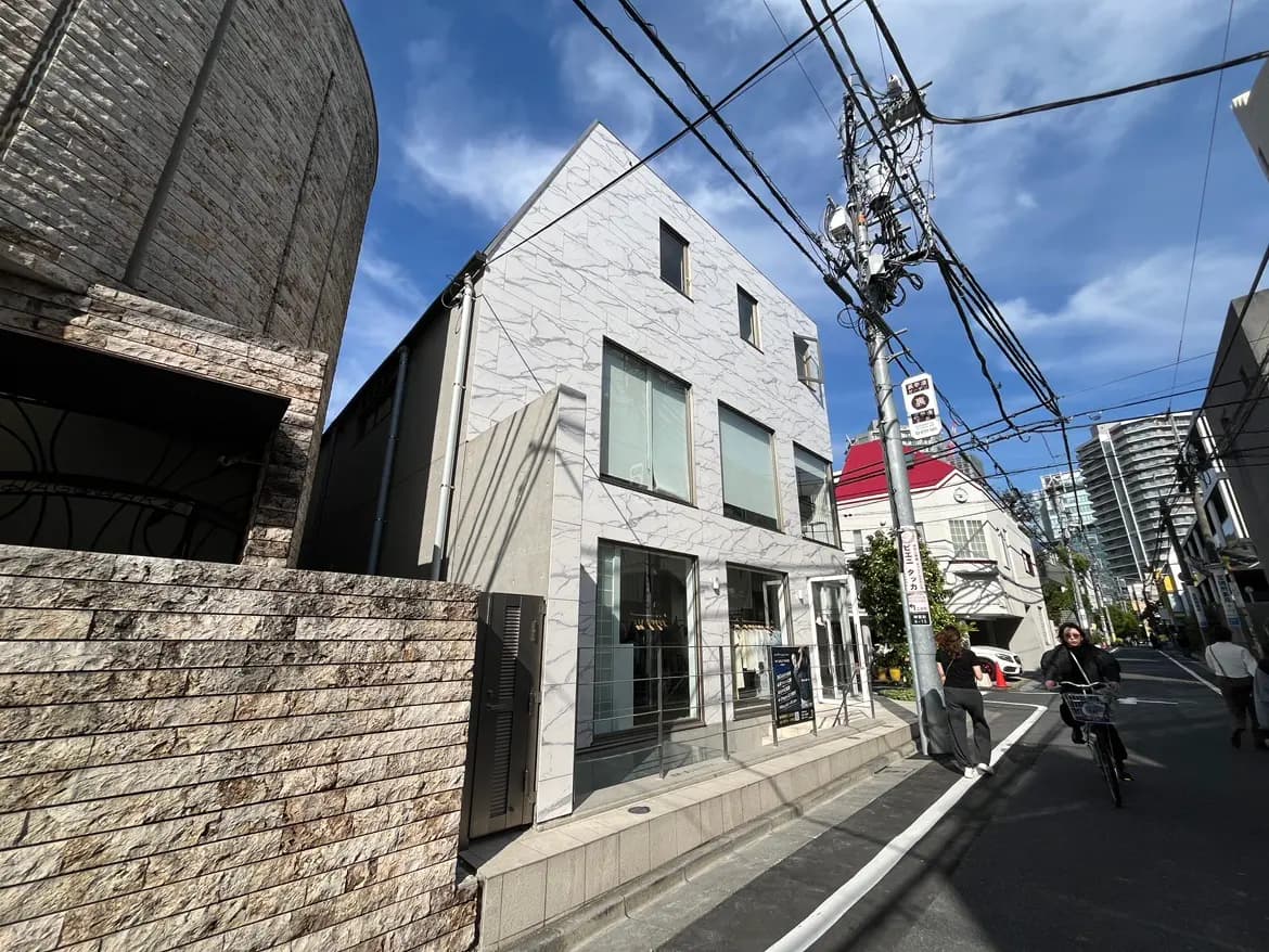 - 都会的なデザインの住宅、白い外壁と石材の特徴、周囲には電線と通行人がいる街並みの風景