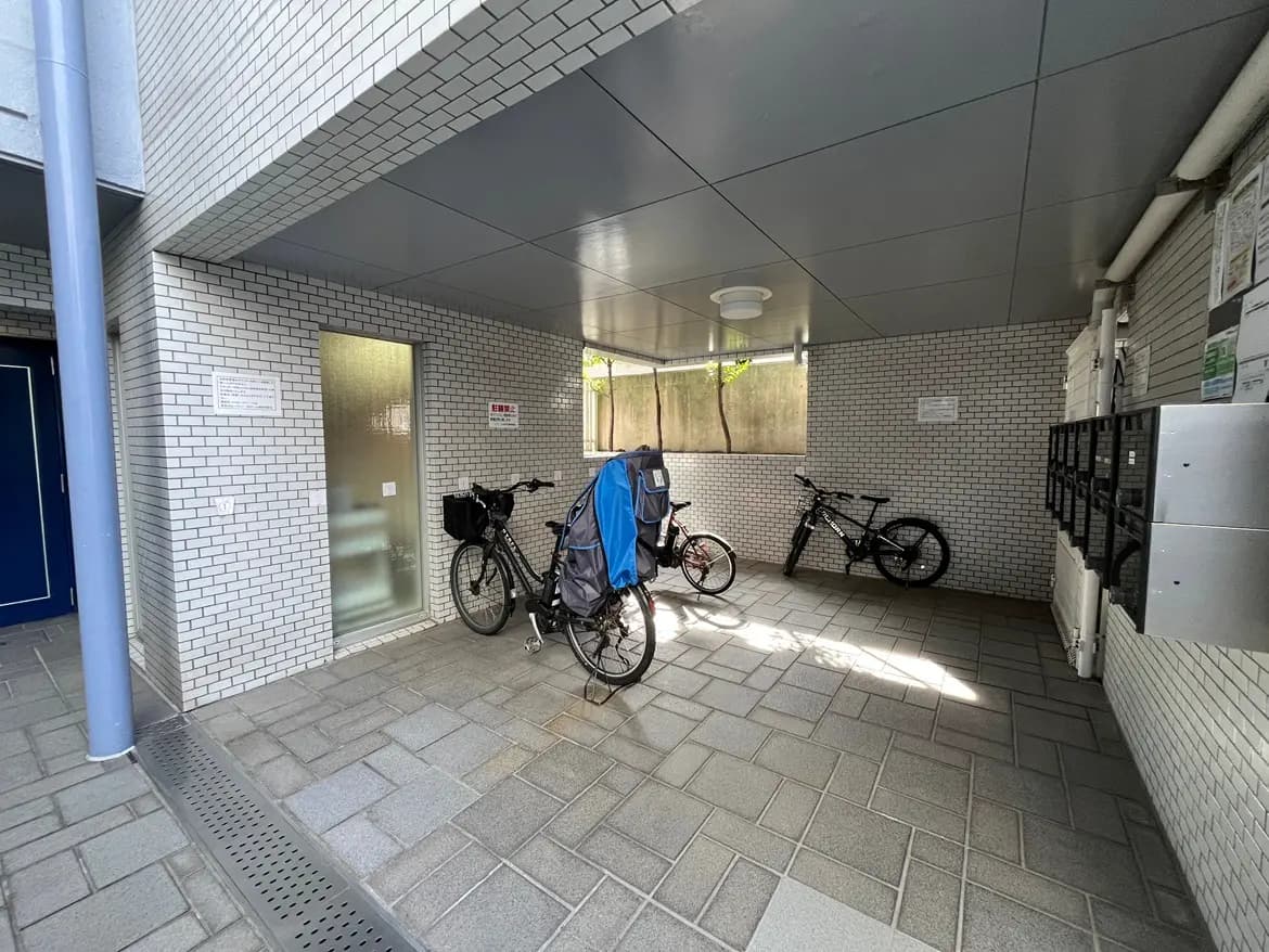 - 自転車が置かれた住宅の屋根付き駐輪場、白いタイルの壁と整然としたスペースが特徴的なインテリア