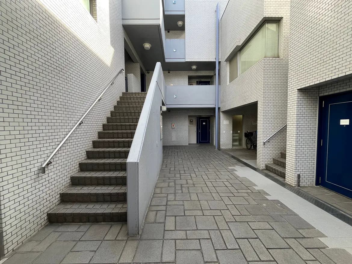 - 都市型住宅の共有スペース、白いタイルの壁と階段が特徴的なエントランスエリアの風景