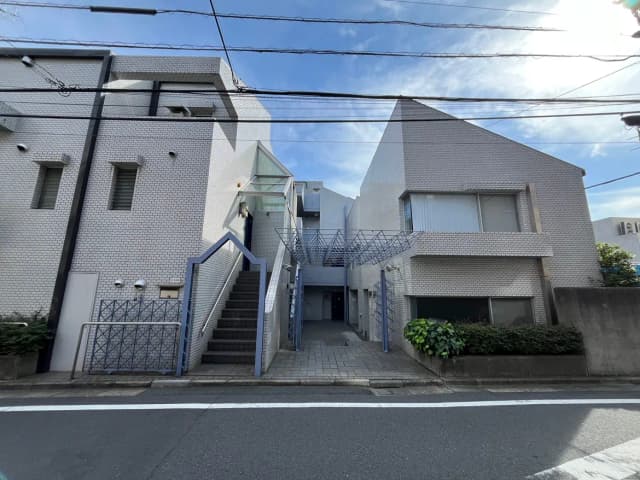 - 近代的な外観の住宅、白いレンガ調の壁、階段と金属製の手すり、青空と電線が見える風景