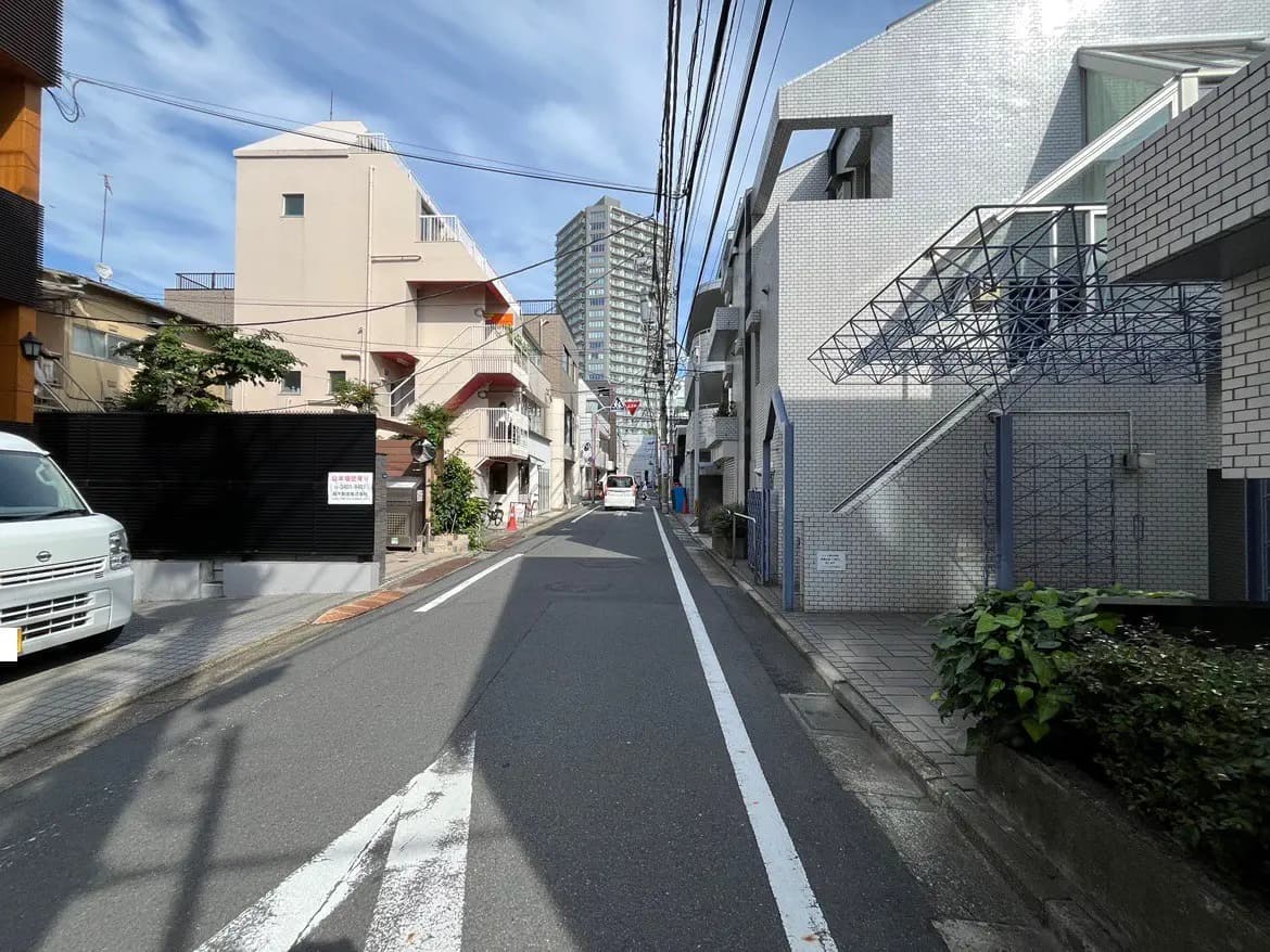 - 都市の住宅街の風景、左右に建物が並ぶ静かな通り、青い空と白い雲が広がる背景
