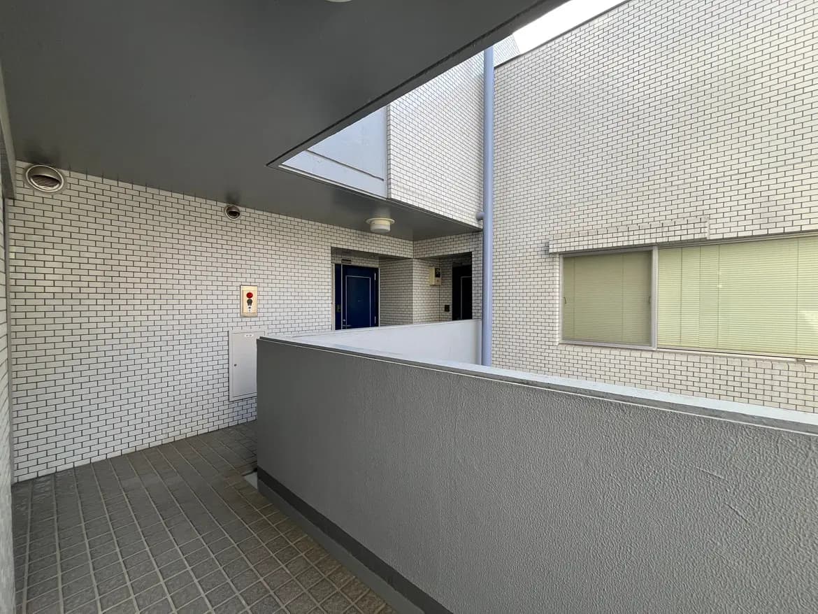 - モダンなデザインのマンションの共用廊下、白いタイルと壁、青い扉、明るい自然光が差し込む空間