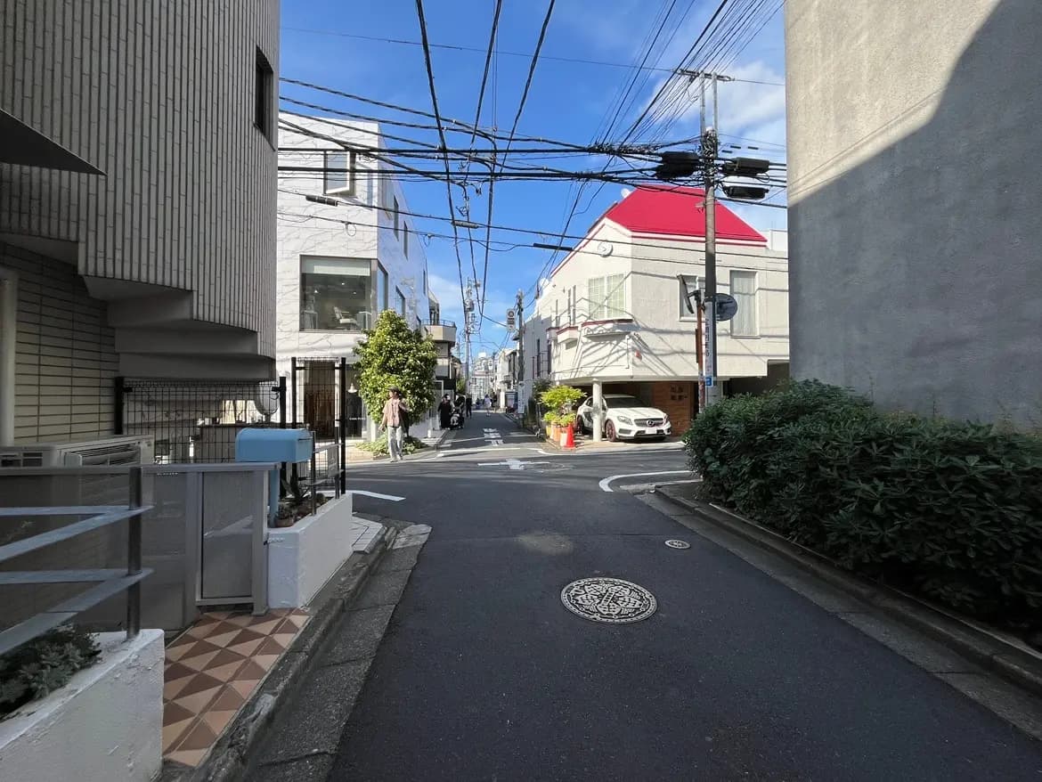- 都市の静かな路地、電線が交差する青空と白い家々、緑の植栽がある風景