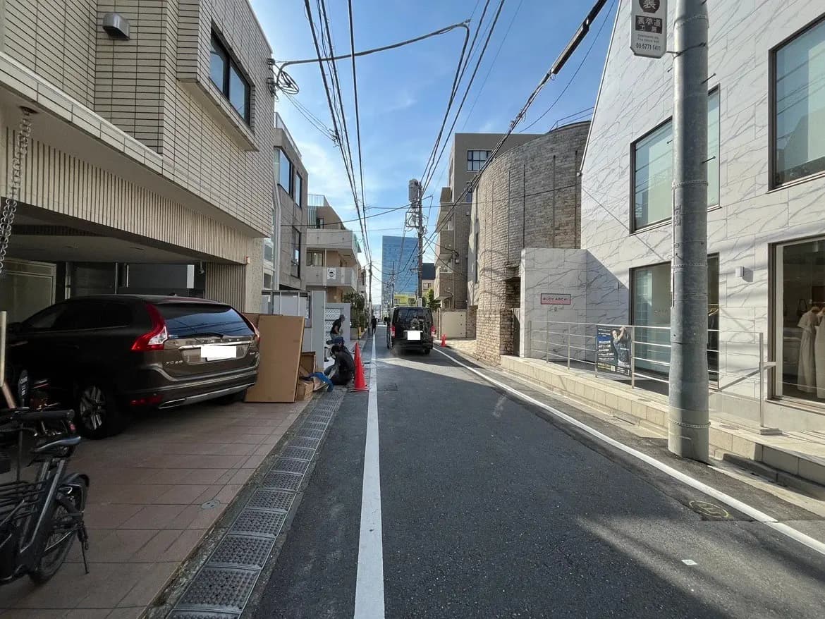 - 都市の路地にある住宅街の風景、自転車と車、青空の下の建物と電線が見える通りの様子