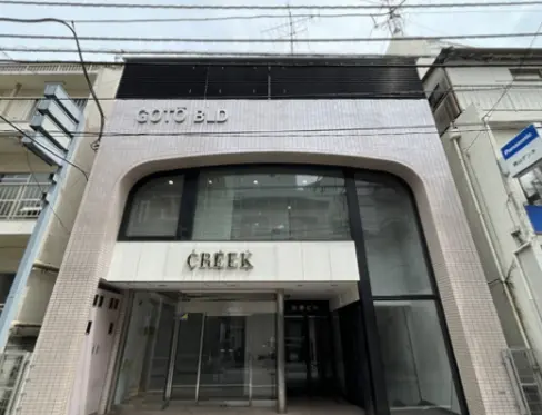 - 都市型の商業ビルの外観、明るいガラスウィンドウと「CREEK」のサインが目立つデザイン