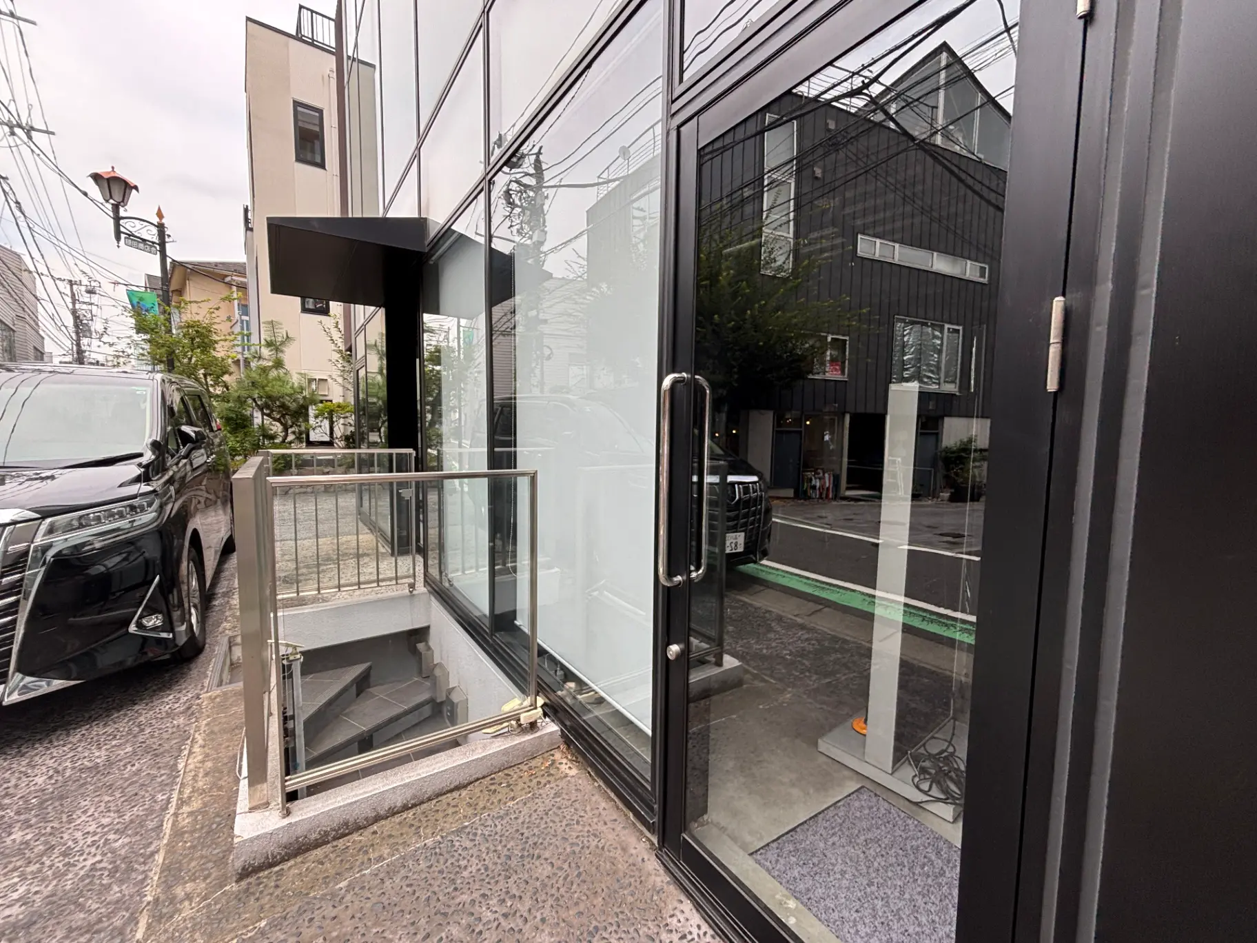 - モダンなビルの入り口、ガラス扉と階段のあるエントランス、黒い車が停まっている風景