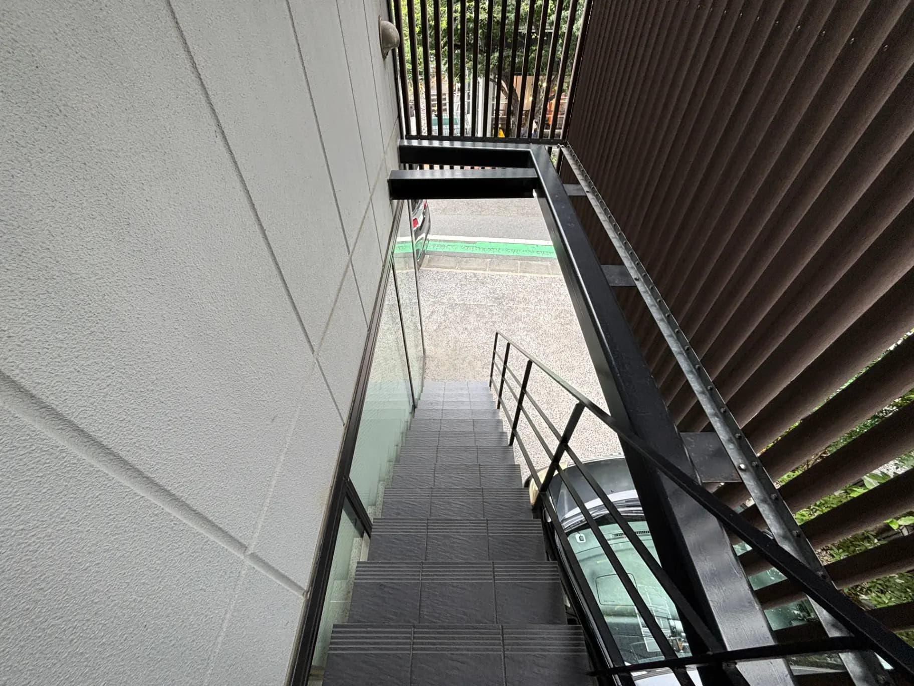 - モダンな建物の階段、ガラスの手すりが見える外部の視点、横には黒い窓枠と壁があるデザイン