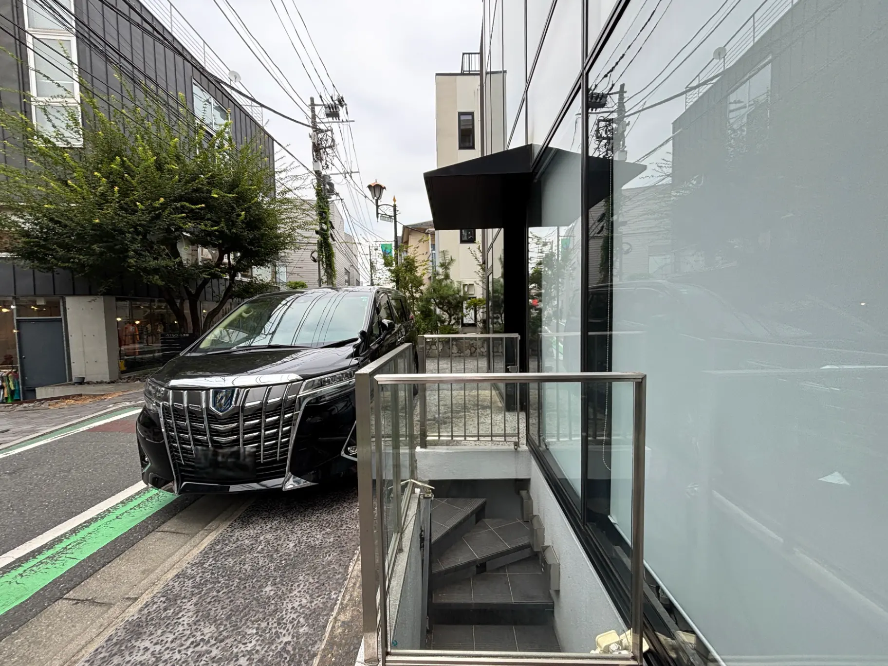 - 黒い高級車が停まるモダンな建物の外観、ガラスの手すりのある階段と周囲の風景が映る都市の風景を背景にした写真