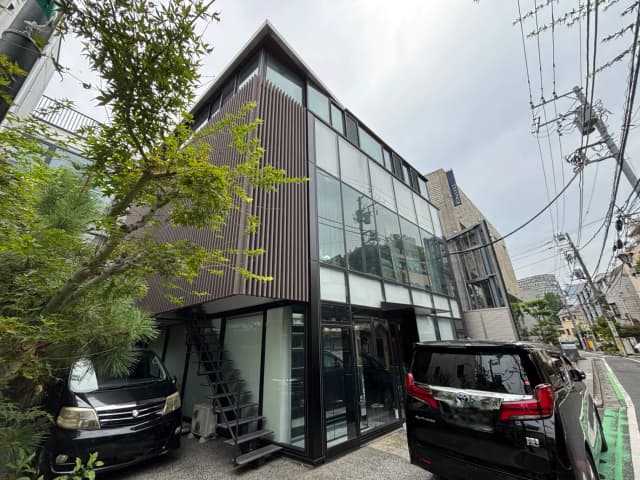 - 近代的なデザインの住宅外観、黒い車と植栽がある立地、ガラスのファサードと階段が特徴的な建物