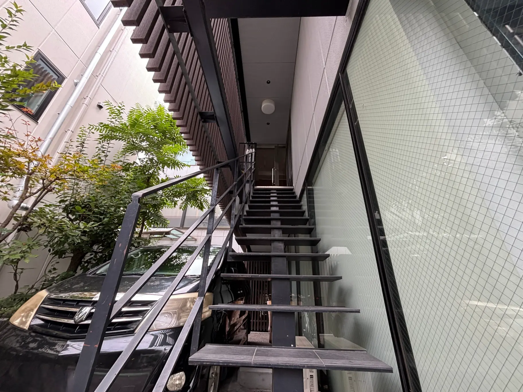 - 鉄骨の階段とガラスの壁に囲まれたエントランス、周囲に緑が生い茂る風景