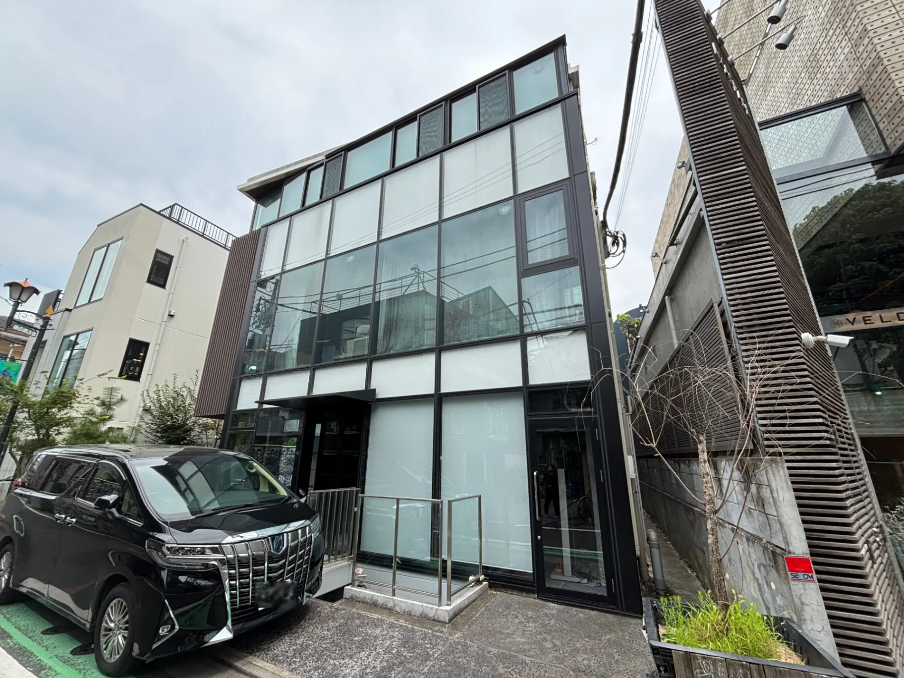 - 近代的なデザインの建物、ガラスファサードと黒い外観、前面に停車した黒い車と周囲の緑がある景観