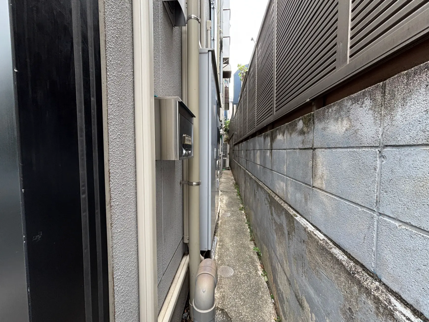 - 狭い街路の風景、隣接する建物の壁と配管、薄暗い照明の環境