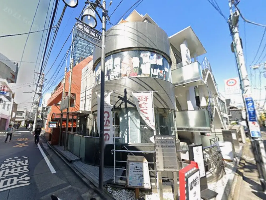 - 魅力的なファサードの店舗、ガラス張りのエントランス、周囲に立ち並ぶビルと明るい青空が広がる街並み