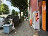 人通りが少ない都市の歩道、左側にごみ箱と車、右側に自動販売機が設置されている風景