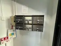 - 複数の郵便受けが取り付けられた壁面の写真、セキュリティボックスとメーターが配置されたエントランスの一部