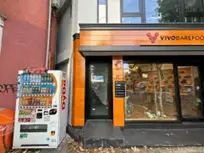 - オレンジ色の木材で装飾されたビストロの外観、隣に並ぶ自動販売機と窓越しに見える店内の様子