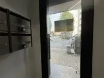 - 鍵付きポストが並ぶエントランスドアの内装、外の景色が見えるガラスドア越しの視界