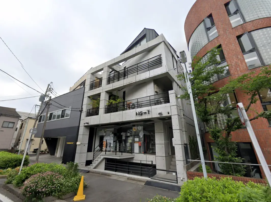 - モダンでコンクリート打ち放しの外観の建物、周囲に緑があり、階段とバルコニーが特徴的なデザインの商業施設