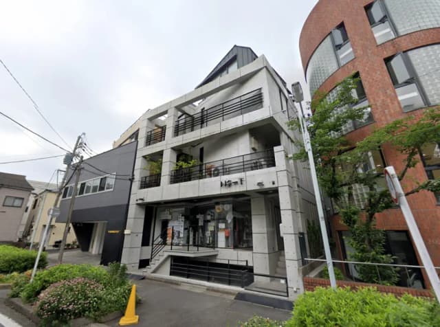 - モダンでコンクリート打ち放しの外観の建物、周囲に緑があり、階段とバルコニーが特徴的なデザインの商業施設