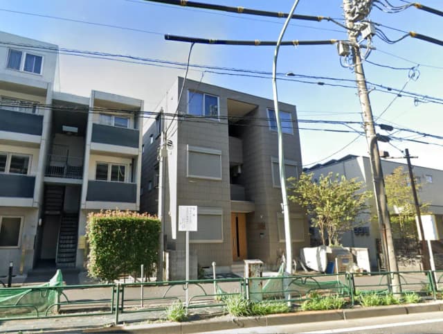 - シンプルでモダンな外観のアパートメント、隣接する建物と緑の植栽が特徴的な街並みの風景