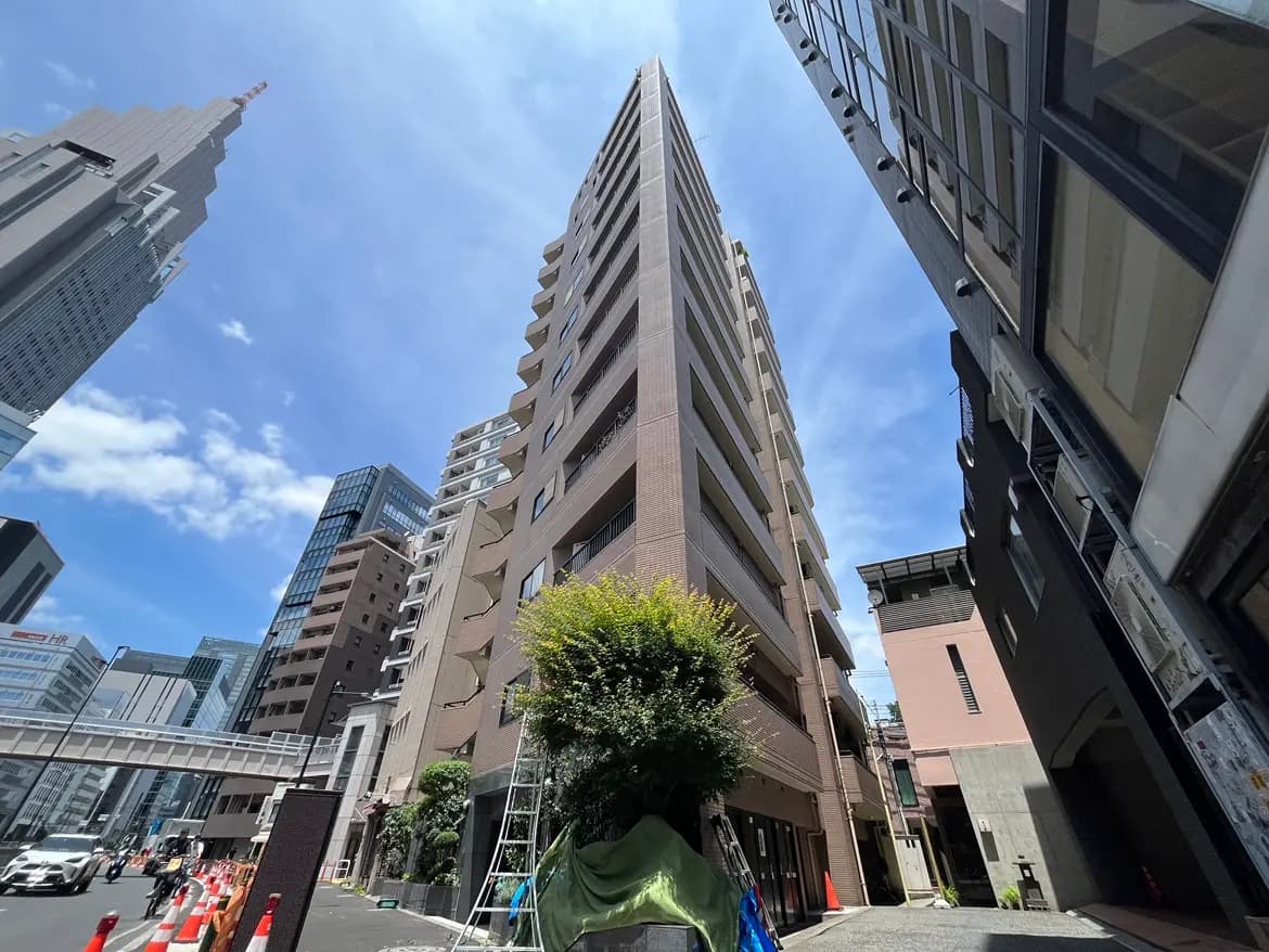 - 高層ビルが立ち並ぶ都市の風景、青空と雲が広がる中、手前に立つ現代的なマンションと道路工事の様子