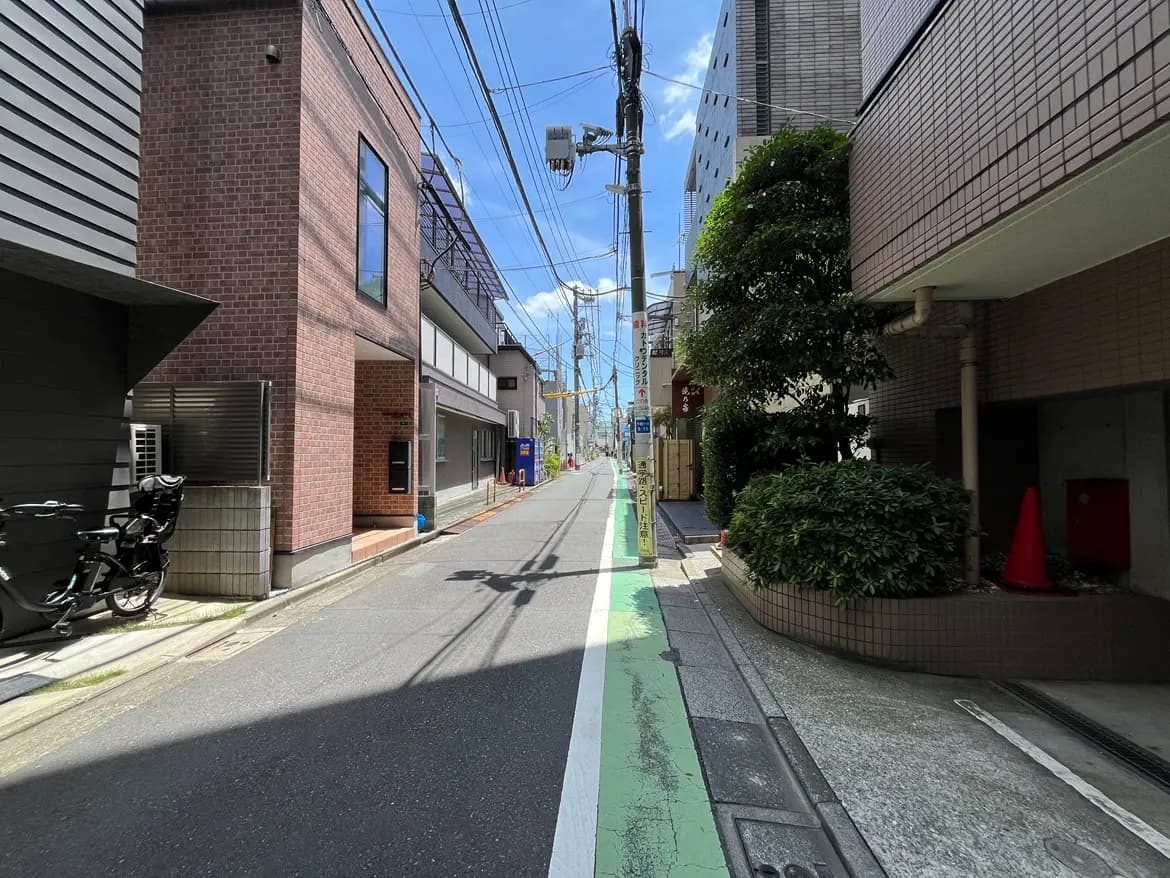 - 明るい青空の下、レンガ造りの建物が並ぶ都市の通り、緑色の自転車専用レーンと周囲の緑豊かな植栽が特徴的な風景