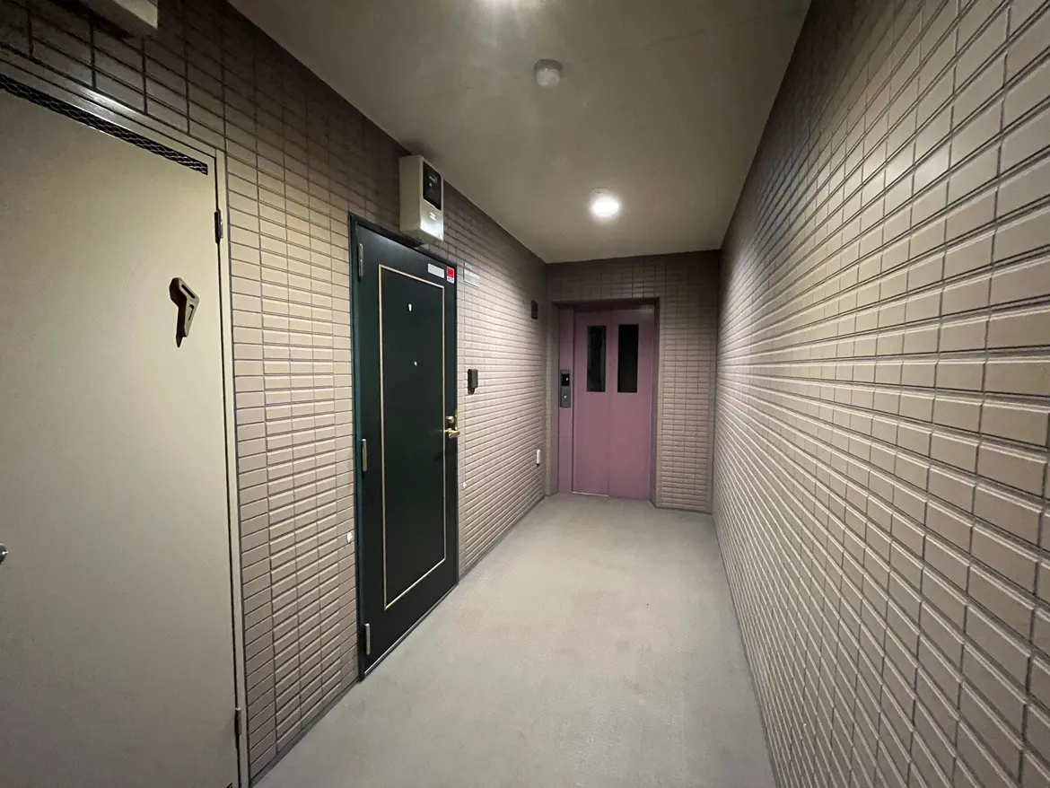 - モダンなエレベーターとドアが並ぶマンションの廊下、壁はタイル張りで明るい照明が点灯しているインテリア