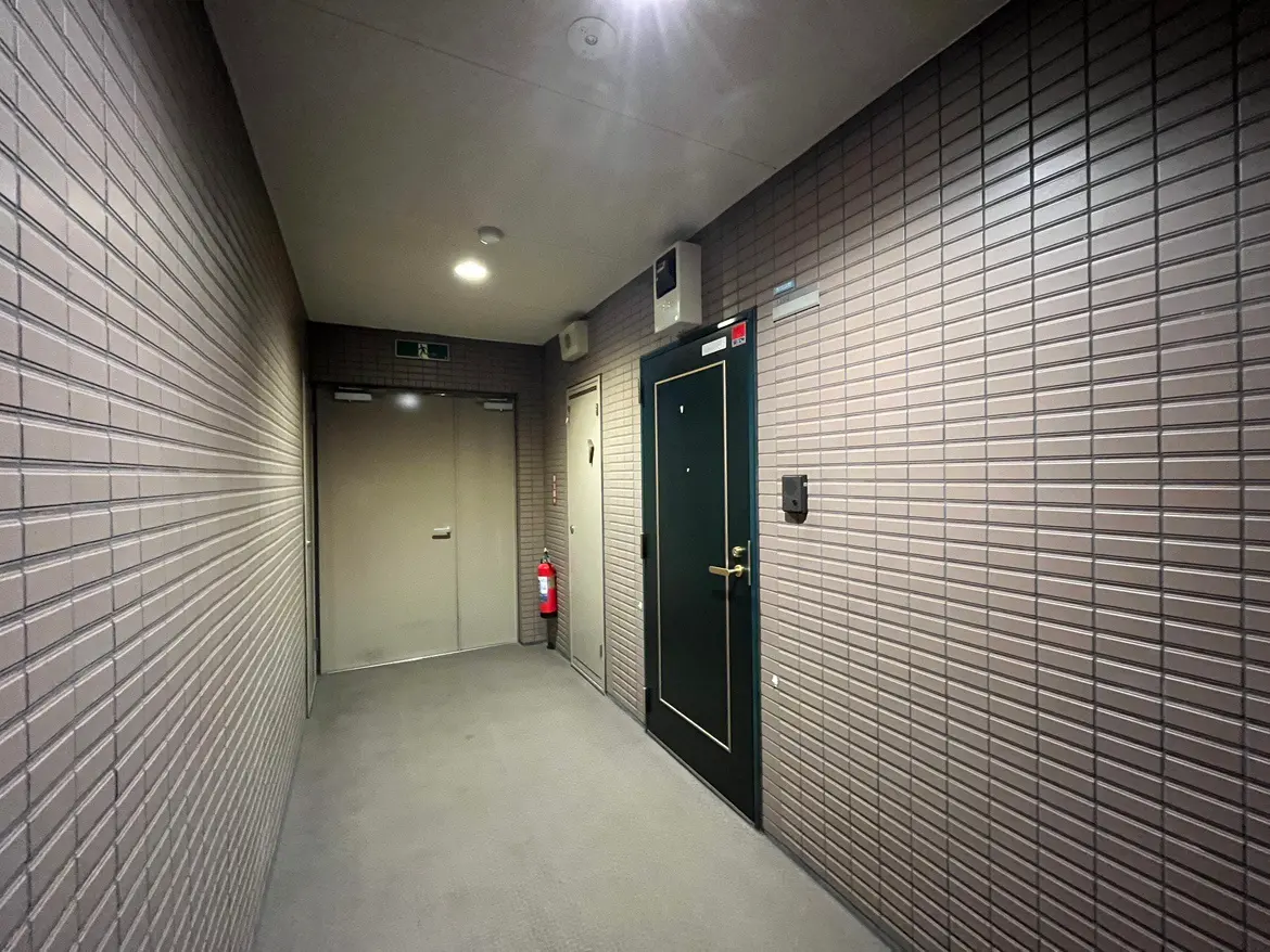 - シンプルで洗練されたデザインの廊下、淡い色合いのタイル壁とドア、火災報知器が設置された安全対策が施された空間