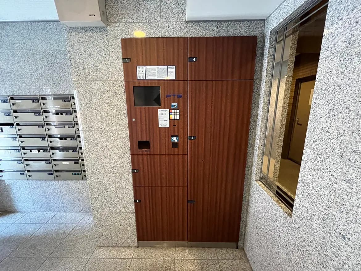 - アパートのエントランスに設置された郵便受けと宅配ボックス、周囲はタイル張りの壁で清潔感のあるインテリア