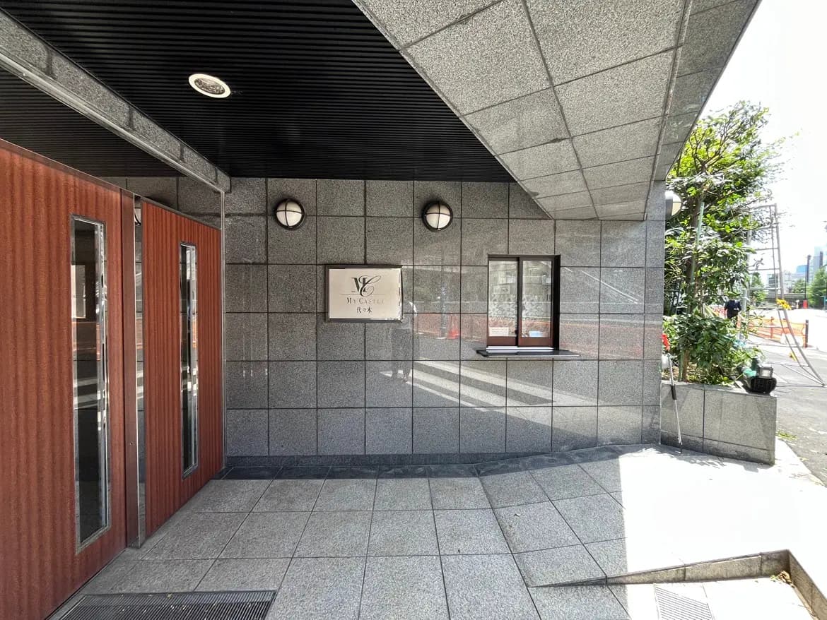 - グレーのタイル張りの建物エントランス、木製の両開きドアと「My Castle」という看板が特徴の玄関口