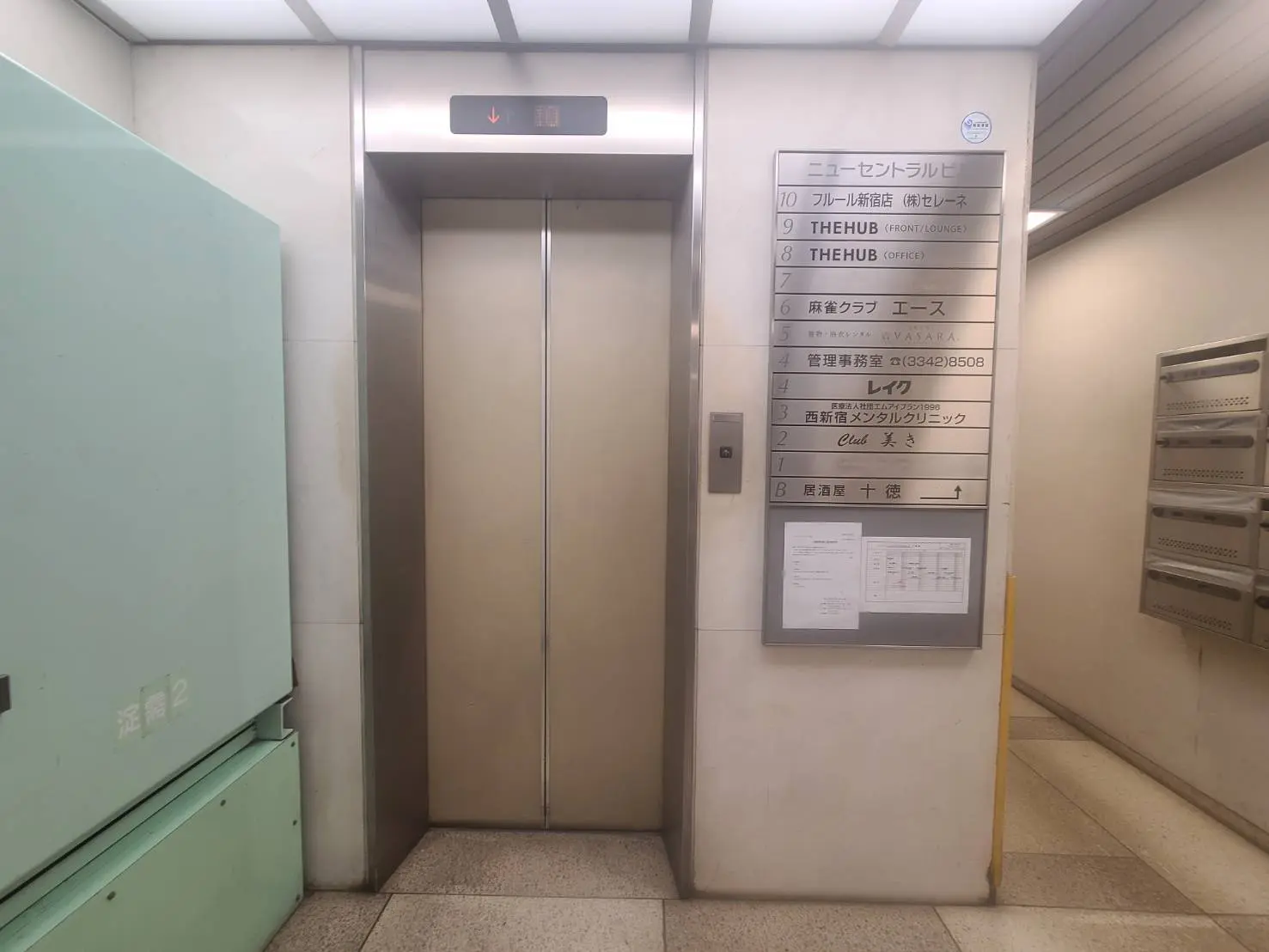 - ニューセントラルビルのエレベーター前の風景、エレベーターの運行表示と周囲の案内板が見えるインテリア