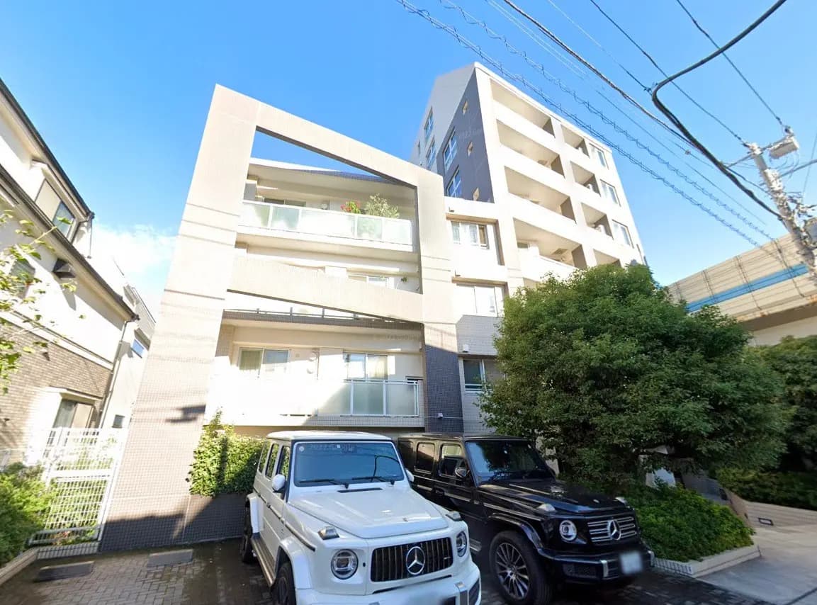 - 現代的なデザインのアパートメントビル、白と黒のSUVが駐車場に並ぶ風景、青空が広がるさわやかな日中の景色
