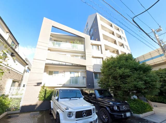 - 現代的なデザインのアパートメントビル、白と黒のSUVが駐車場に並ぶ風景、青空が広がるさわやかな日中の景色
