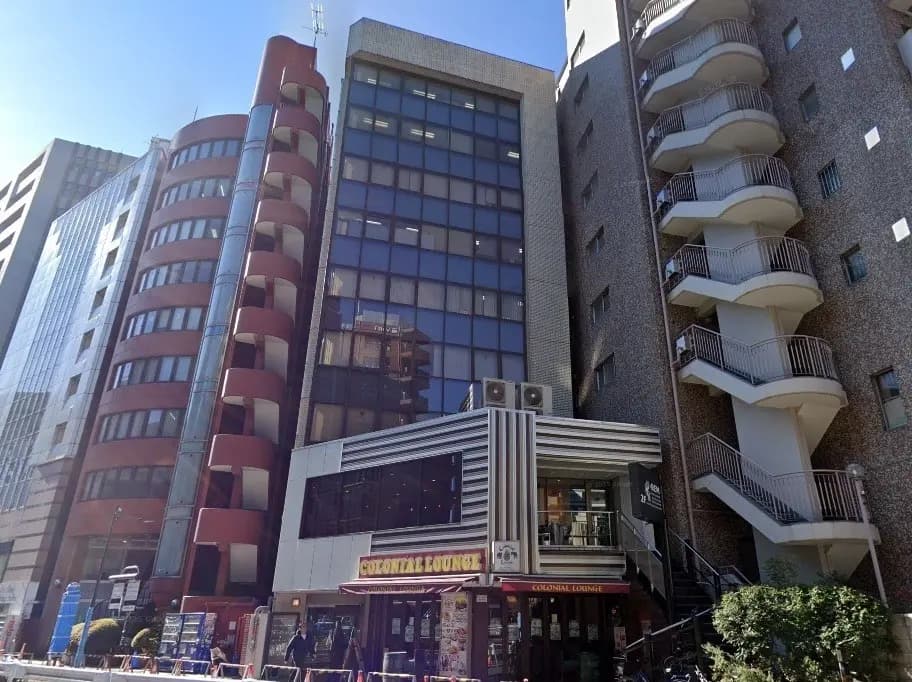 - 現代的なデザインのビルが立ち並ぶ都市風景、カラフルな外観の飲食店「コロニアルラウンジ」が目立つ場所