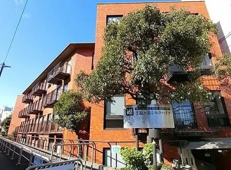 - 暖かいレンガ造りの外観を持つアパートメントビル、周囲には緑豊かな樹木と看板が配置された風景