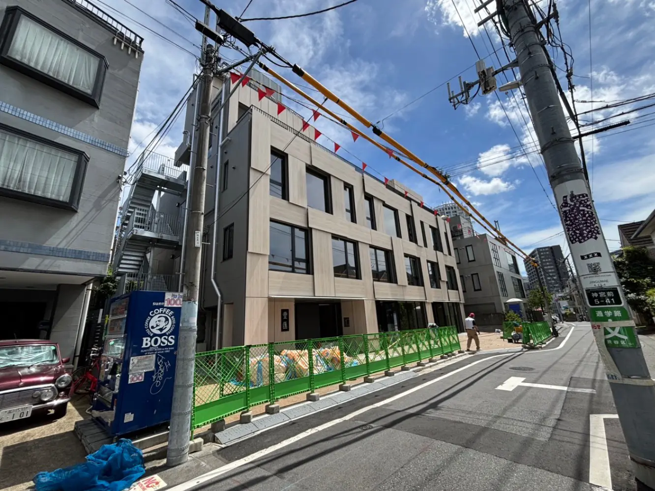 - 近代的な外観の建物、周辺に工事中の様子、青空と電柱が映る都市の風景