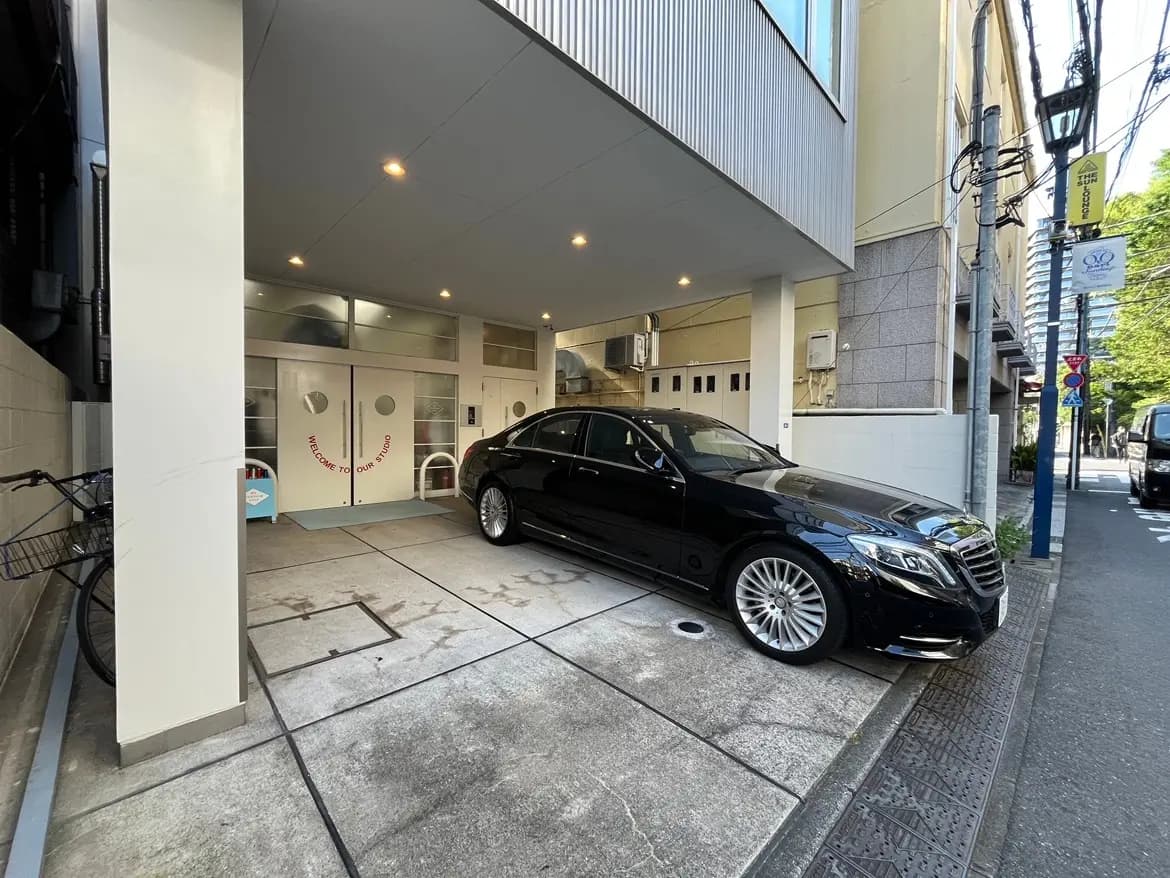 - 黒い高級車が停まっている建物のエントランス、周囲には自転車と街灯が見える都市の風景