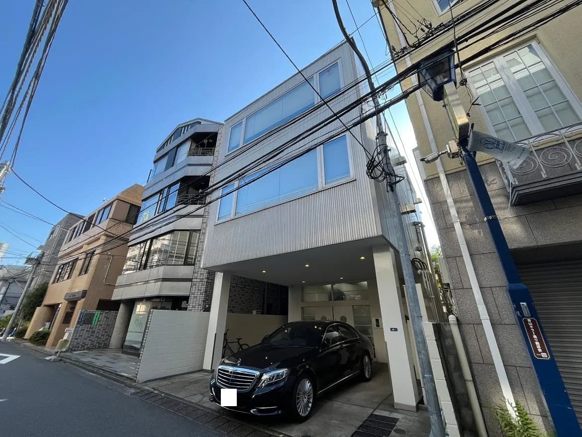 - 現代的な外観の住宅、隣接する建物と電線、整備された歩道と黒い高級車が駐車されている様子