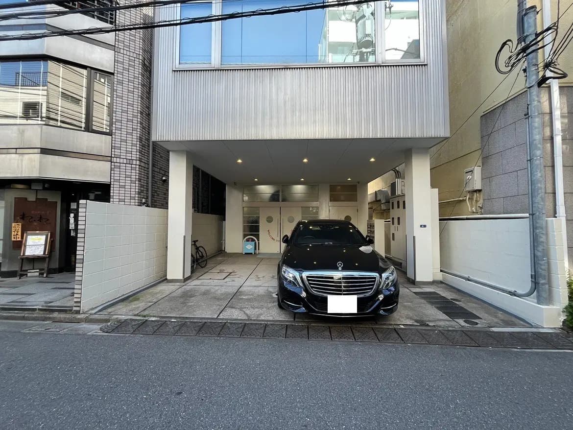 - モダンな建物の前に停車している黒いメルセデス車、隣に自転車が置かれた駐車場の風景