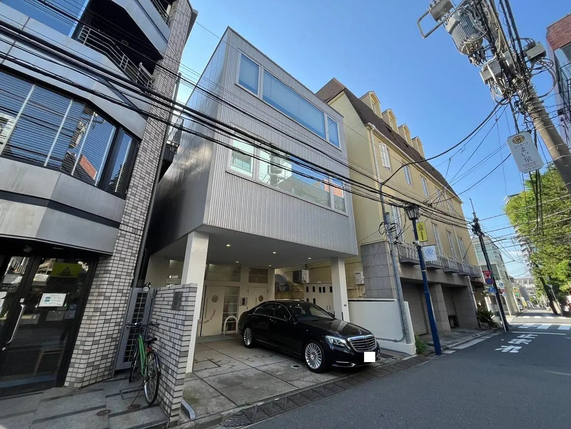 - モダンなデザインのビル外観と黒い高級車、周囲の電線が見える街並みの風景