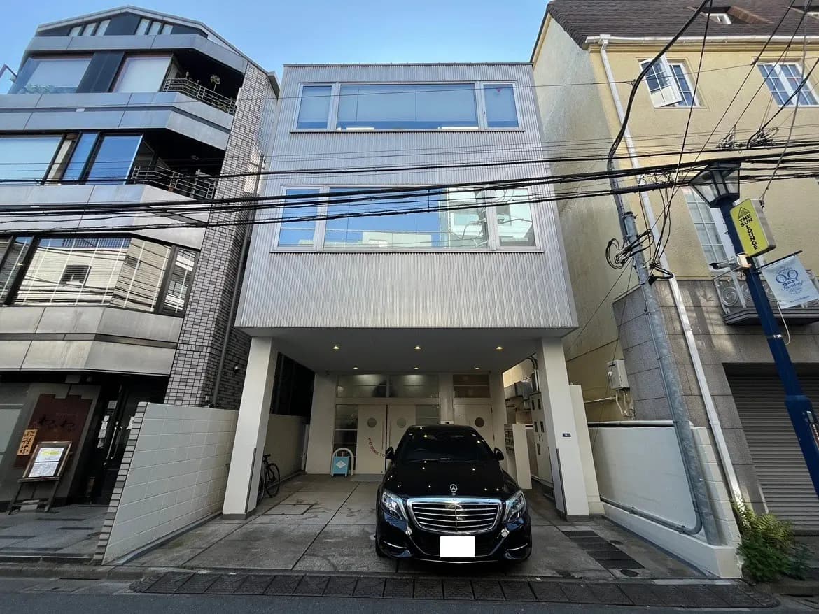 - モダンなデザインの3階建て住宅、黒い車が駐車場に停まっている外観、隣接する建物とのコントラストが目を引く景観