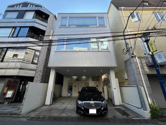 - モダンなデザインの3階建て住宅、黒い車が駐車場に停まっている外観、隣接する建物とのコントラストが目を引く景観