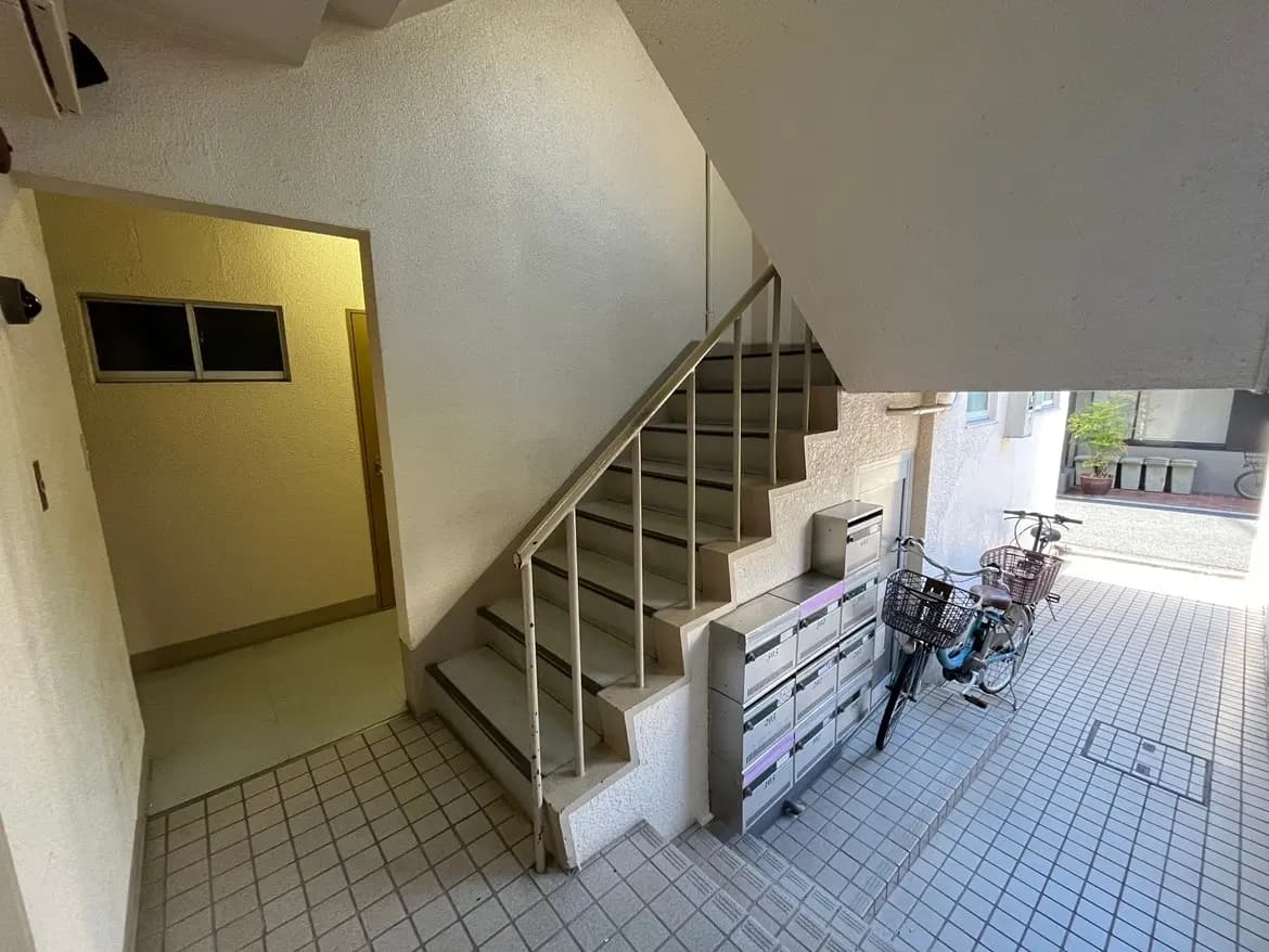- 建物の階段とエントランス、郵便受けが並び、片側には自転車が停まっているシンプルなインテリアの風景